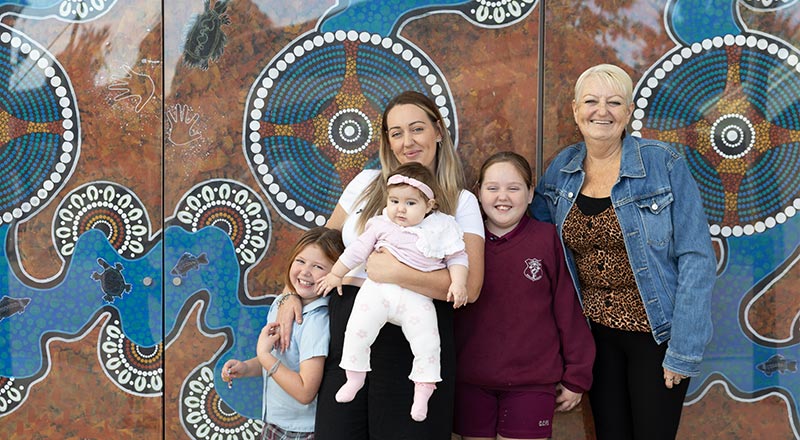 Mum, three children, and grandma standing in front of painted Aboriginal mural on mothers day