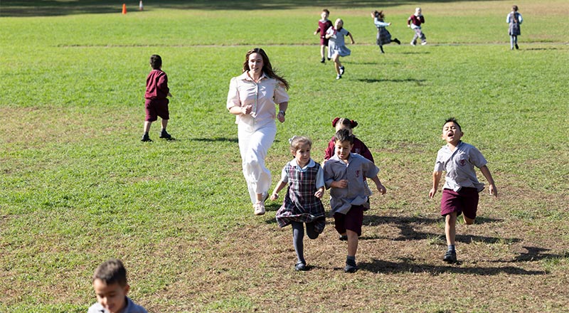 Children and teacher running through sports field
