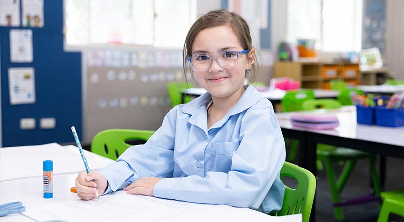 Student, wearing glasses, writing into workbook