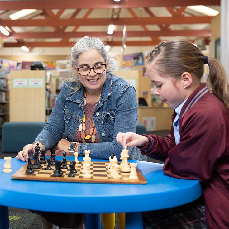 Teacher and student playing chess in library